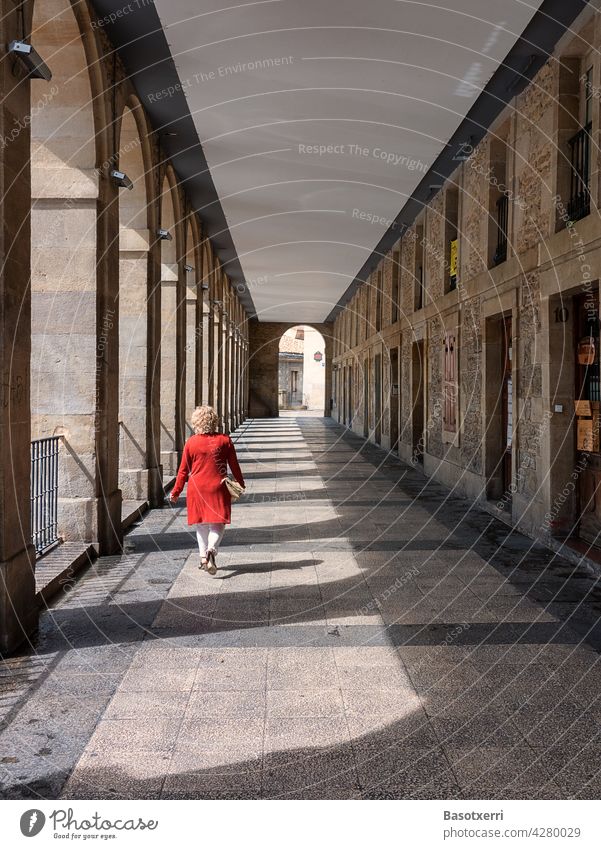 Frau in rotem Mantel durchkreuzt den Arkadengang in der Altstadt. Los Arquillos, Vitoria-Gasteiz, Baskenland, Spanien Vitoria Gasteiz Passage roter Mantel