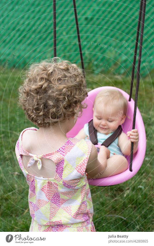 Fünf Jahre altes Mädchen hilft ein Jahr alten Cousin in rosa Schaukel; Baby lächelnd Schwestern Cousins und Cousinen Hilfsbereitschaft pendeln Eimerschaukel