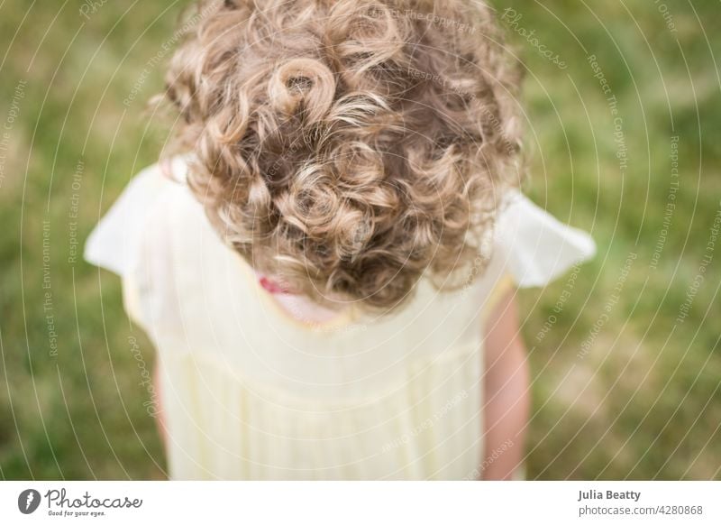 Junges Mädchen mit kurzen blonden lockigen Haaren, das ein gelbes Vintage-Blumenmädchenkleid trägt; Ansicht von Oberkopf und Haar Rolle wellig natürlich Kind