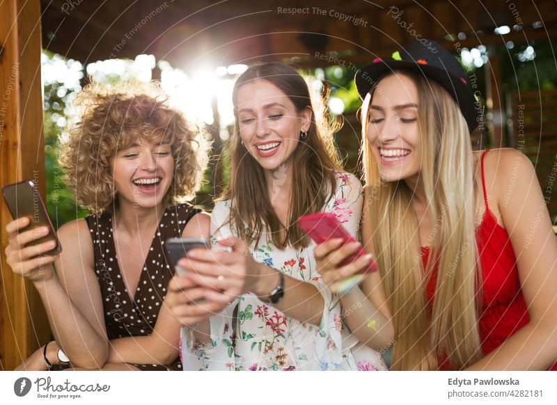 Glückliche junge Frauen haben Spaß mit Smartphones Sonnenuntergang Sommer Menschengruppe Zusammensein lässig schön attraktiv Mädchen drei Personen Freunde