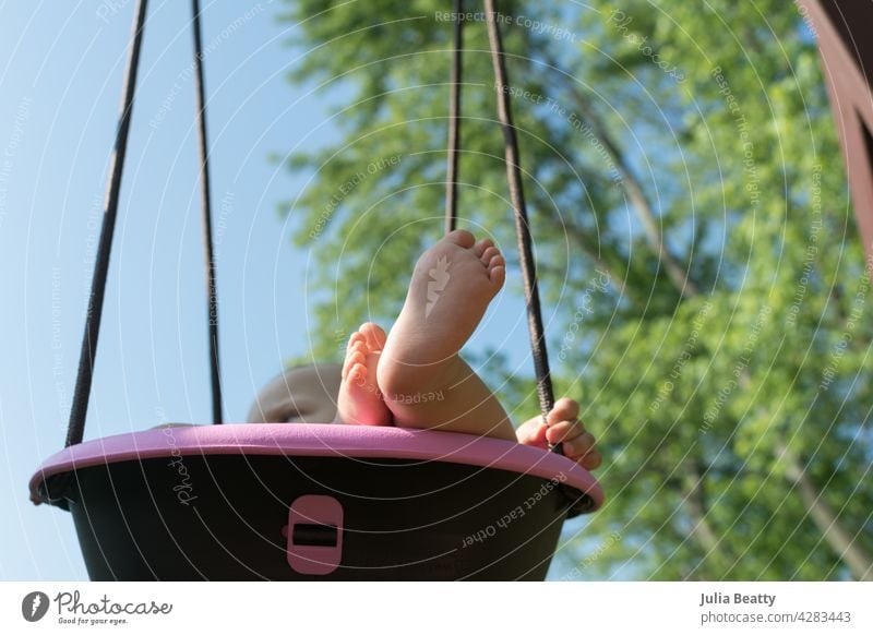 Blick auf das in der rosa Eimerschaukel schaukelnde Baby; mollige Babyfüße und -hände sichtbar pendeln ein Jahr alt Kleinkind Kind Zehen Fuß Swing-Set