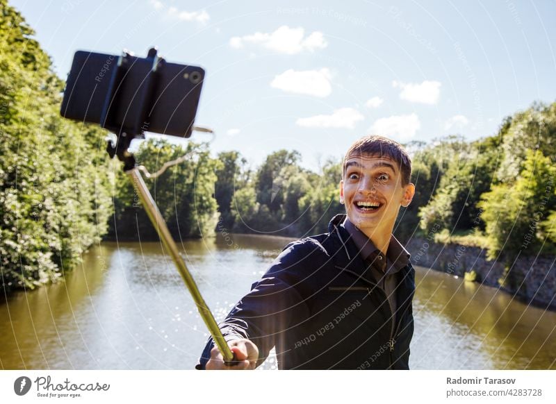 junger Mann macht Selfie mit einem Selfie-Stick männlich kleben Fotokamera Selbst Gesicht Porträt Glück Freizeit Hintergrund Person machen Smartphone Hand