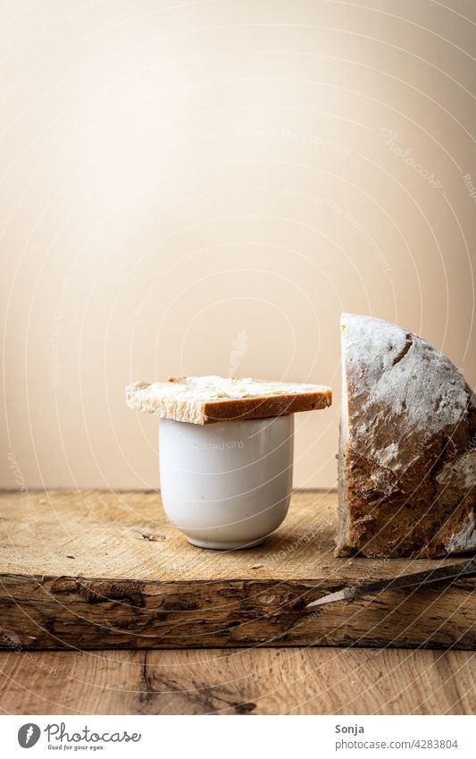 Eine Scheibe Brot mit Butter auf einer Kaffeetasse Frühstück Holztisch Morgen Lebensmittel Ernährung rustikal ländlich beiger Hintergrund lecker natürlich