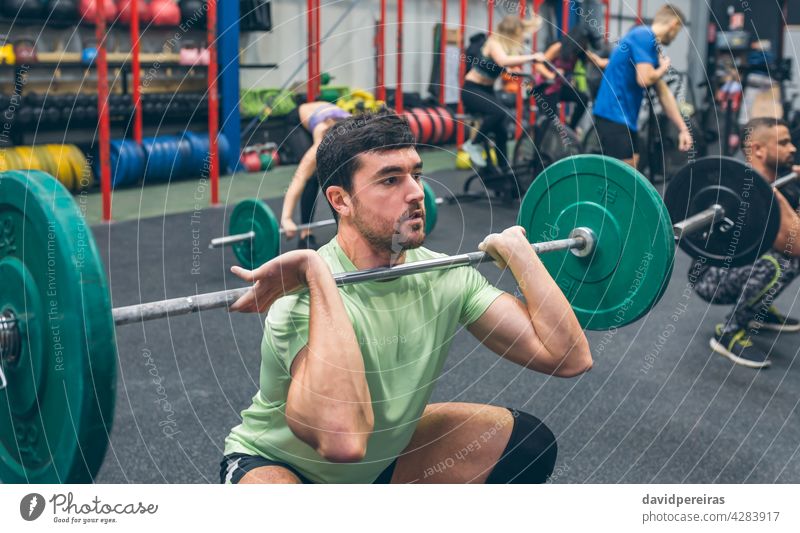 Mann übt Gewichtheben in der Turnhalle Sportler anstrengen Kurzhantel Cross-Training Tatkraft Heben Greifen Überwindung Überkopfhocke selbstbewusst Zug Stärke