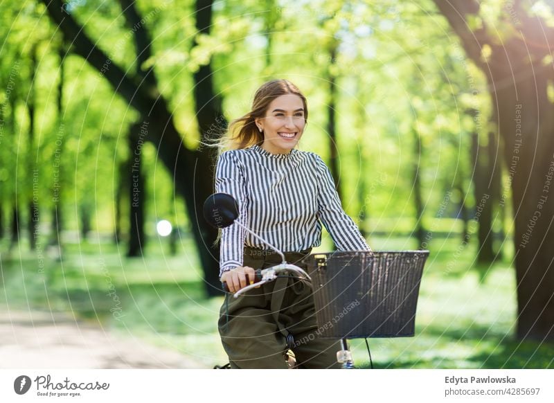 Junge Frau radelt durch den Park grün Bäume Natur Frische genießend Lifestyle jung Erwachsener Menschen lässig Kaukasier positiv Glück Lächeln attraktiv schön