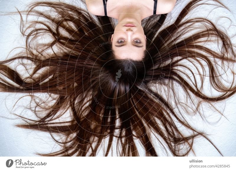 Schöne junge Frau liegend auf dem weißen Hintergrund mit langen weit verbreiteten ausgestreckten Haar Ausgestreckt Behaarung Lügen braun schön Mode Haarpflege