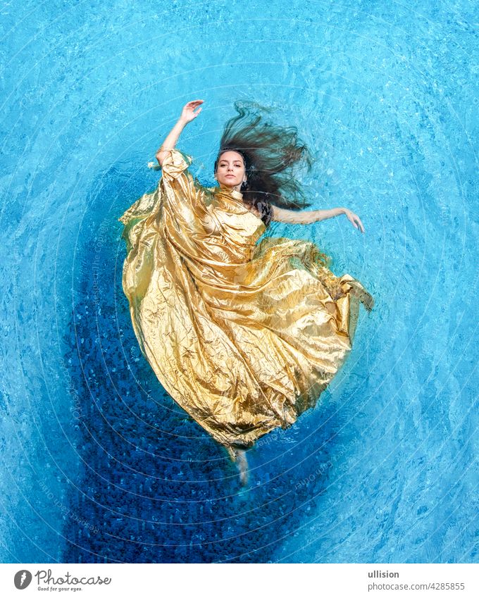 Draufsicht auf eine schöne junge sexy Frau in goldenem Kleid, Abendkleid, Handtuch schwebt schwerelos elegant schwimmen im Pool Wasser Stoff Meerjungfrau blau