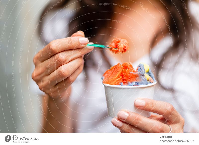 Frau hält einen Becher mit regenbogenfarbenem Eis Eiscreme Hand Essen hispanisch frisch Straßenessen Menschen smartwatch Hände Frucht Beteiligung lgbt Farben