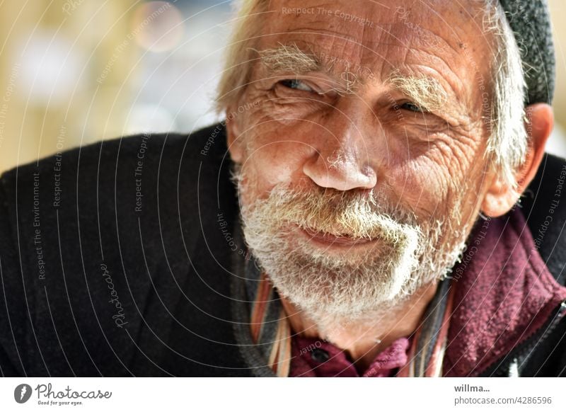 Verschmitzt lächelnder Mann mit weißem Bart Porträt bärtig Senior weißhaarig Vollbart Gesicht verschmitzt gewitzt schmunzeln Runzeln freundlich gutgelaunt