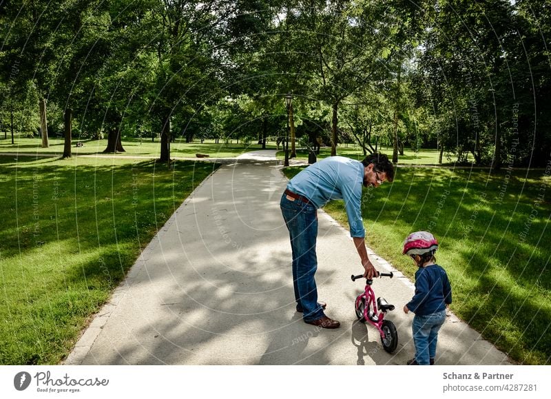 Papa übt mit Kind Laufrad fahren Tochter Elternzeit Ausflug Helm lernen Park Natur Vater Zusammensein Familie & Verwandtschaft Mädchen Sommer