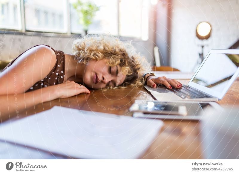 Junge Geschäftsfrau schlafend an ihrem Schreibtisch in einem Büro Business Geschäftsleute Geschäftsmann Menschen Kaukasier Frau im Innenbereich informell lässig