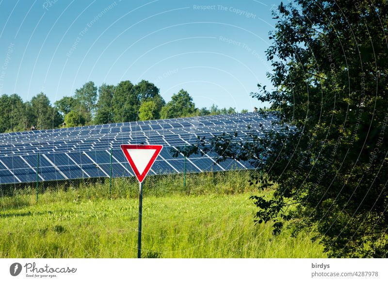 Vorfahrt achten - Schild vor einem Solarpark umgeben von Bäumen und Wiese. Symbolbild, vorrangig regenerative Energien fördern. Solarförderung Photovoltaik