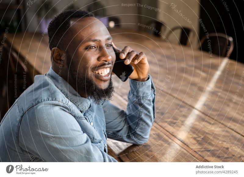 Lächelnder junger Schwarzer, der mit seinem Smartphone spricht Mann reden Telefonanruf positiv Kommunizieren Gespräch heiter Anschluss diskutieren froh Inhalt