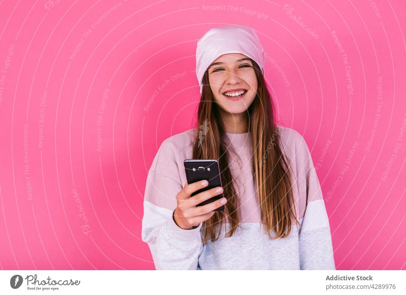Glücklicher Teenager auf Smartphone auf rosa Hintergrund Jugendlicher Krebs Browsen Kopftuch Frau Onkologie tausendjährig Porträt Chemotherapie benutzend krank