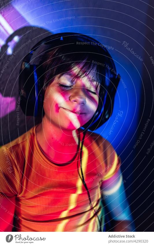 Zufriedenes Mädchen, das ein Tablet benutzt und über Kopfhörer Musik hört zuhören Tablette Browsen Apparatur heiter Inhalt Augen geschlossen neonfarbig Licht