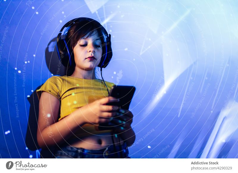 Kleines Mädchen, das ein Tablet benutzt und über Kopfhörer Musik hört zuhören Tablette Browsen Apparatur neonfarbig Licht Kind lässig Surfen Anschluss genießen