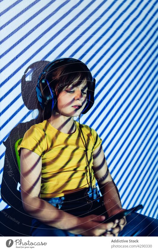 Kleines Mädchen, das ein Tablet benutzt und über Kopfhörer Musik hört zuhören Tablette Browsen Apparatur neonfarbig Licht Kind lässig Surfen sitzen Anschluss