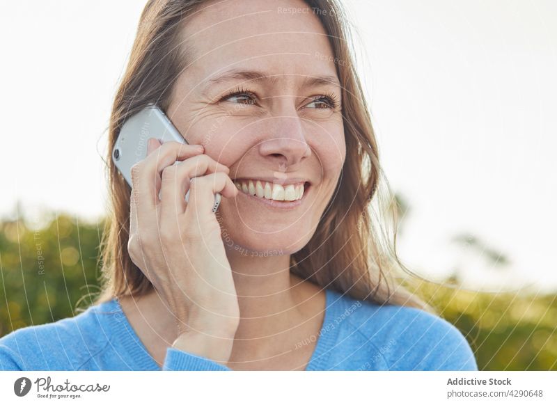 Frau telefoniert in der Nähe von Sträuchern auf der Straße Telefonanruf Funktelefon Lächeln Buchse Großstadt Garten Erwachsener modern Pflanze gealtert