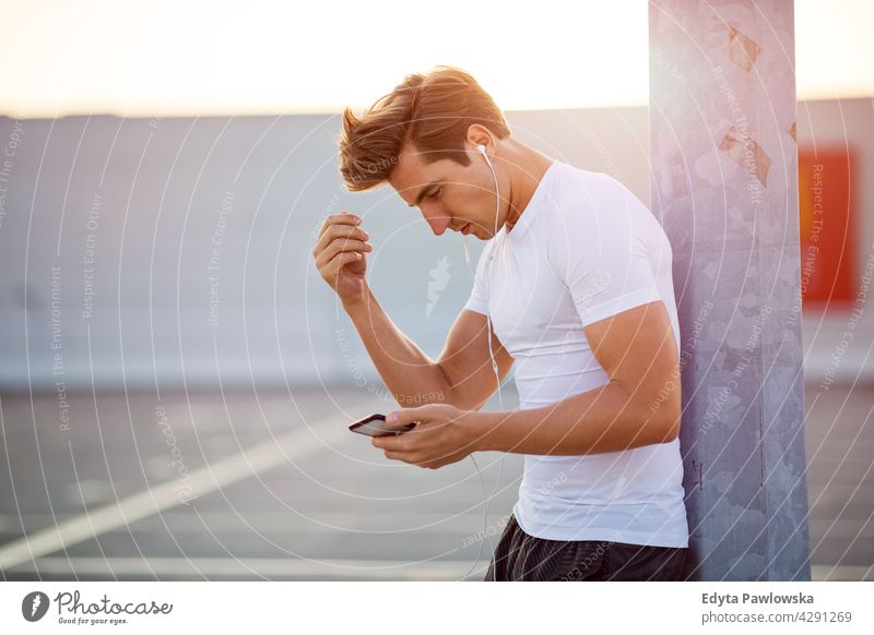 Junger Mann überprüft sein Smartphone vor dem Training MP3-Player Musik hören Kopfhörer App Radio Monitor Verlauf Handy Technik & Technologie Jogger Läufer