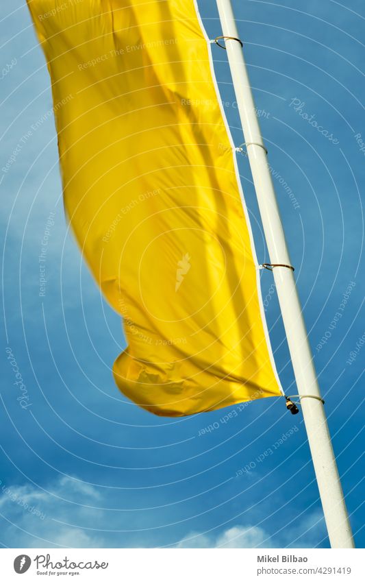 gelbe Flagge an einem Mast über blauem Himmel. Fahne winkend Wind windig Ornament bunt Farben Hintergrund Gewebe Stoff Material Muster Kultur farbenfroh Objekt