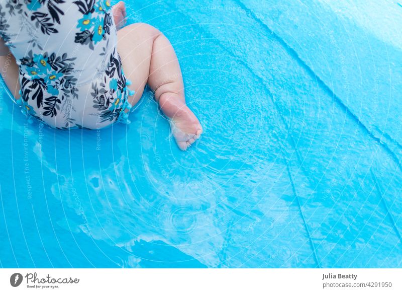 Junges Baby sitzt in einem blauen aufblasbaren Schwimmbecken; Kleinkind trägt einen geblümten Badeanzug Wassersicherheit Sonnensicherheit Pool Pool aufblasen