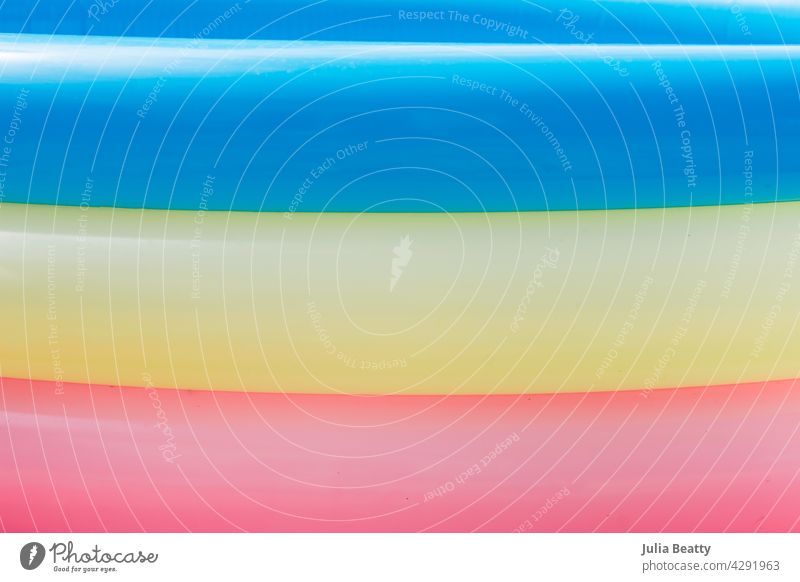 Sommer: Nahaufnahme der Seite des aufblasbaren Pools mit blauen, gelben und rosa Ringen aufgeblasen rund geschwollen traditionell Bonbon hell verblüht abstrakt