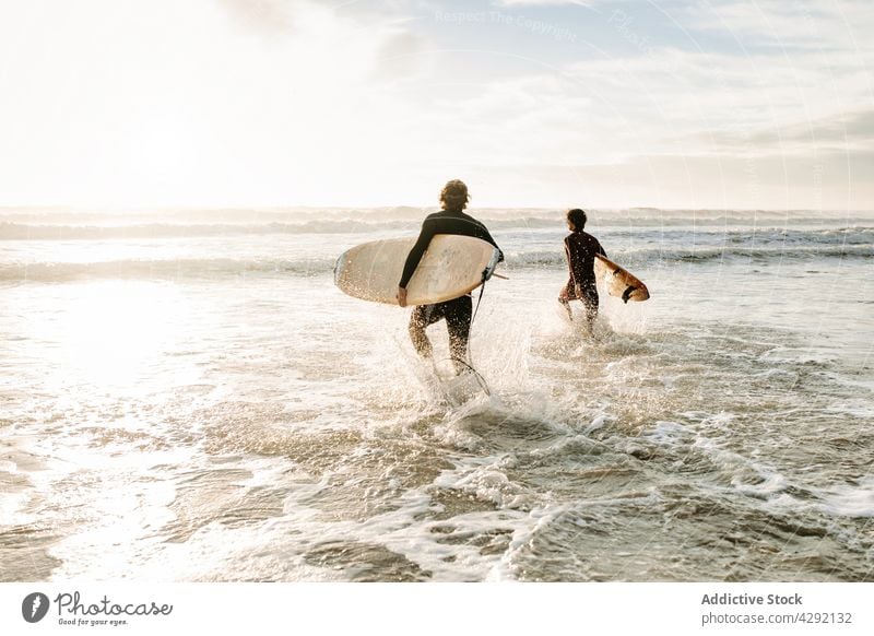 Anonyme Surferfreunde am Strand mit Surfbrettern Freunde Natur Sonnenuntergang winken im Freien Neoprenanzug Meeresküste Zusammensein Brandung Sportler MEER