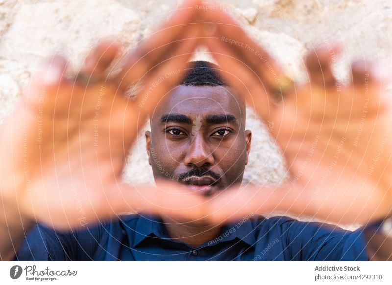 Schwarzer Mann zeigt Dreiecksgeste mit Händen an der Wand ernst gestikulieren manifestieren Hände gefaltet Straße selbstbewusst allein Afroamerikaner schwarz
