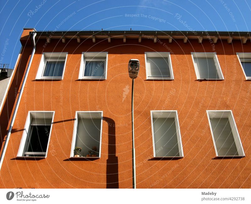 Sanierte Hausfassade in Orange mit Straßenlaterne vor blauem Himmel im Sonnenschein in Offenbach am Main in Hessen Altbau Wohnhaus Fassade Fenster Rollladen