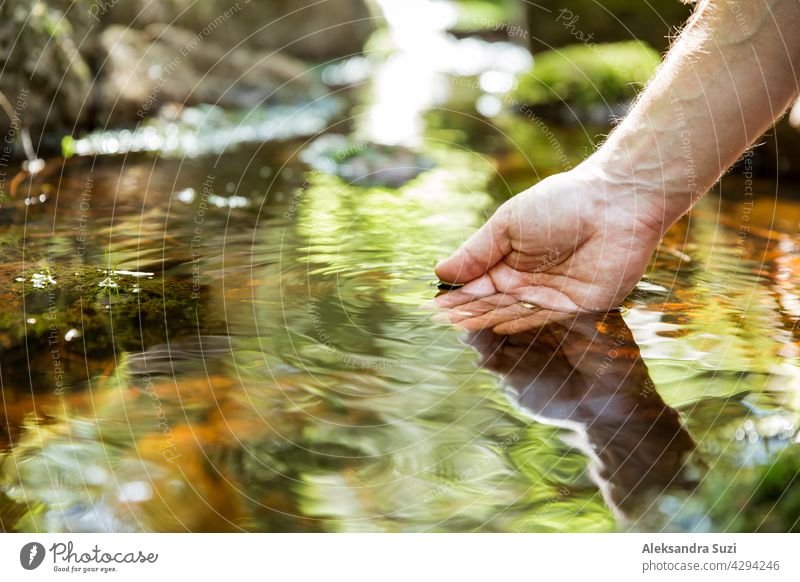 Mann nimmt klares Wasser aus einem Bach im Wald. Nahaufnahme der Hand. Nuuksio-Nationalpark, Finnland. Sonniger Sommertag im Wald. Schöne Quelle Wasser läuft in Felsen.