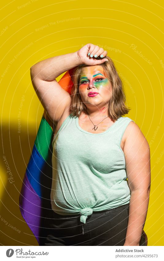 Plus-Size-Frau mit LGBT-Flagge, die den Kopf berührt lgbt Fahne Stolz Make-up kreativ Tastkopf abstützen farbenfroh hell Regenbogen körperpositiv mehrfarbig