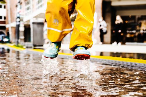 Kind springt fröhlich in eine Pfütze Wasser Spiegelung Asphalt Straße nass Reflexion & Spiegelung springen Regen Boden schlechtes Wetter Wolken Spielen fuesse