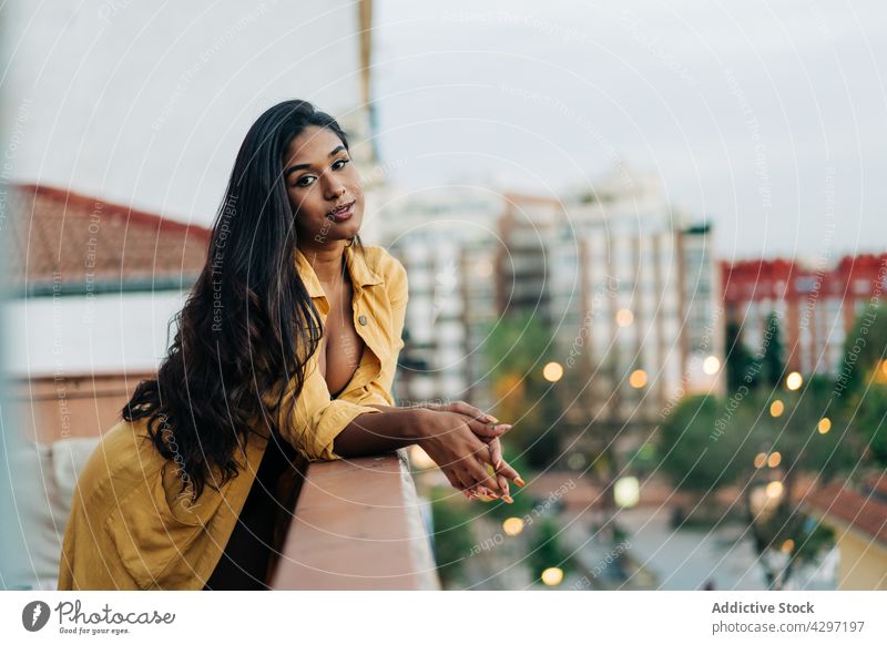 Hispanische Frau beim Chillen auf dem Balkon am Abend ruhen fettarm Reling Großstadt Wochenende heimwärts Straße lässig ethnisch jung hispanisch Terrasse trendy