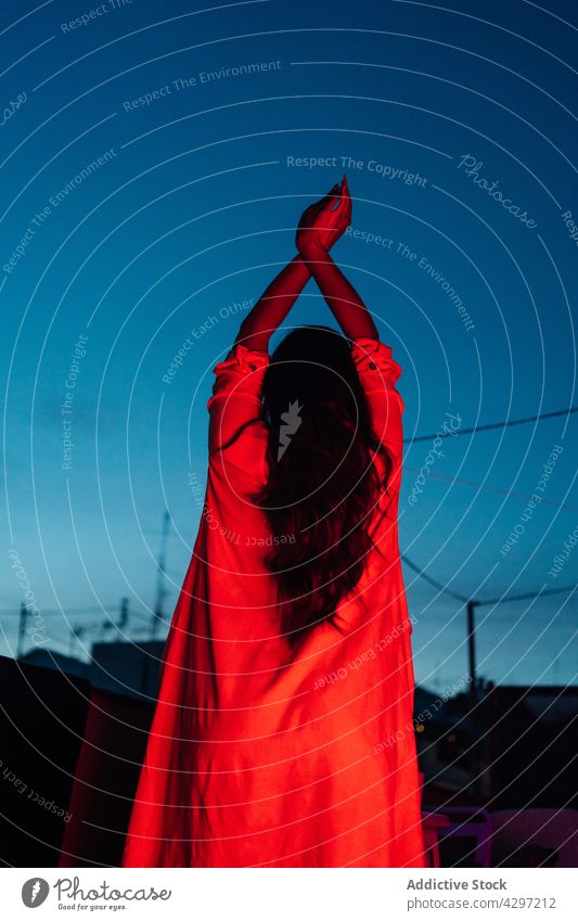 Anonyme Frau auf Terrasse bei Nacht ruhen neonfarbig Rotlicht Stil dunkel jung leuchten sich[Akk] entspannen Freude ethnisch Arm angehoben attraktiv positiv