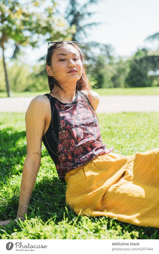 Sanftmütige asiatische Frau ruht sich auf dem Rasen im Park aus verträumt sanft feminin charmant angenehm Sommerzeit Wiese Porträt nachdenken Ornament Tattoo
