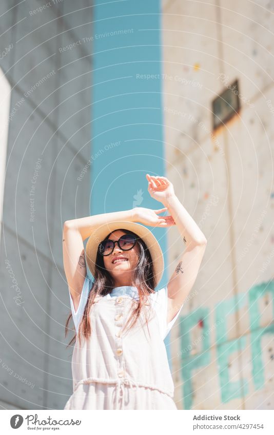 Stilvolle asiatische Frau mit Sonnenbrille in der Stadt Inhalt Tattoo romantisch Individualität Lifestyle Arm angehoben heiter Hut Lächeln genießen Sommer