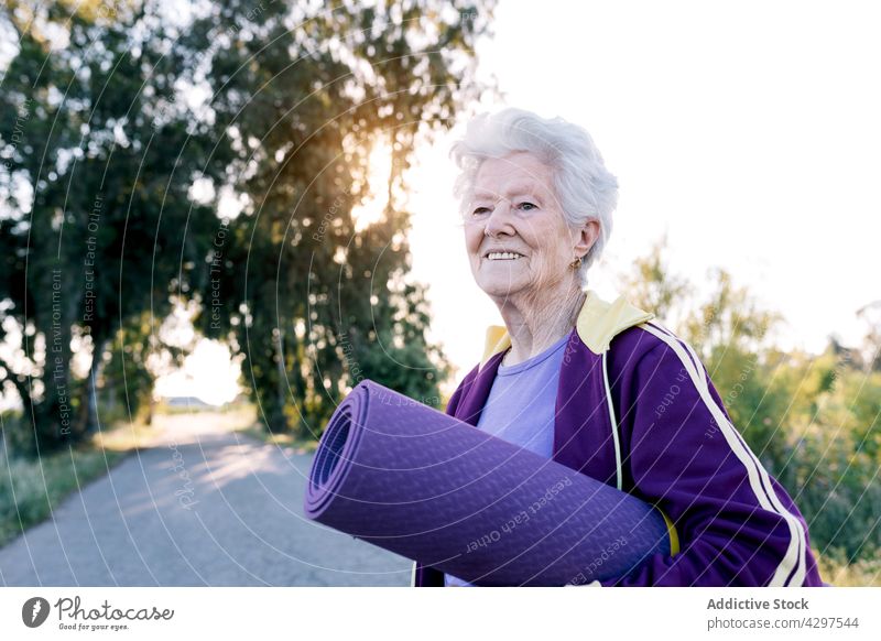 Glückliche ältere Sportlerin mit Matte auf dem Lande Training Fitness Landschaft Morgen Lächeln Unterlage führen Gesundheit Sportbekleidung Frau gealtert Senior
