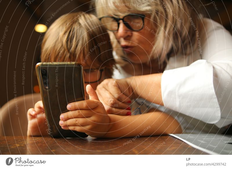 Junge, der eine Brille trägt und unter Aufsicht eines Erwachsenen ein Display eines Handys betrachtet Kindererziehung Homeschooling Surfen im Netz Anschluss
