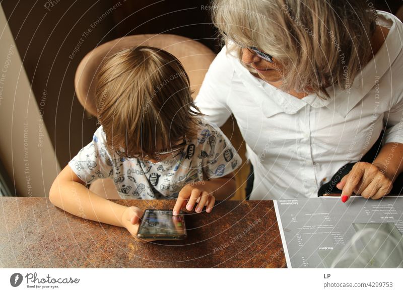 Junge, der eine Brille trägt und unter Aufsicht eines Erwachsenen ein Display eines Handys betrachtet Kindererziehung Homeschooling Surfen im Netz Anschluss