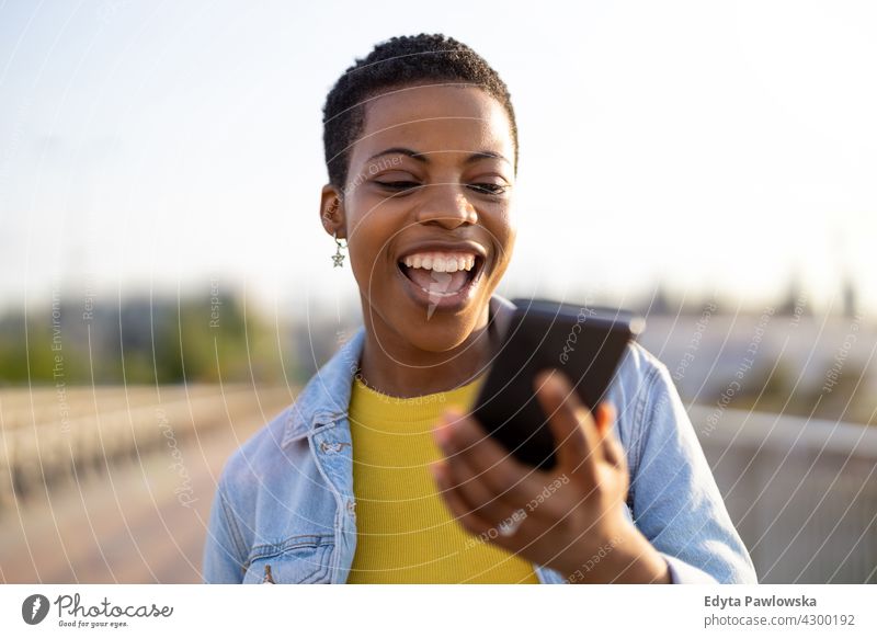 Lächelnde junge Frau mit Smartphone im Freien Afro-Look stolz echte Menschen Stadtleben Afroamerikaner Afrikanisch Schüler schwarz Ethnizität sonnig