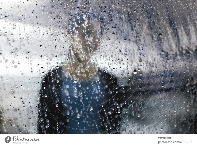 Ein trauriges Mädchen, verschwommen vor dramatischem Himmel,  hinter einer transparenten Plane voller Regentropfen Melancholie nachdenklich einsam Tropfen Hülle