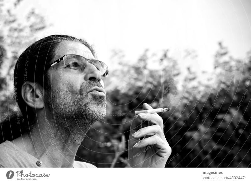 Rauchen. Seitenansicht des Mannes mit langen Haaren und Bart der raucht. Rauch ausatmen. Raucher hält rauchende Zigarette in der Hand Sucht Erwachsene