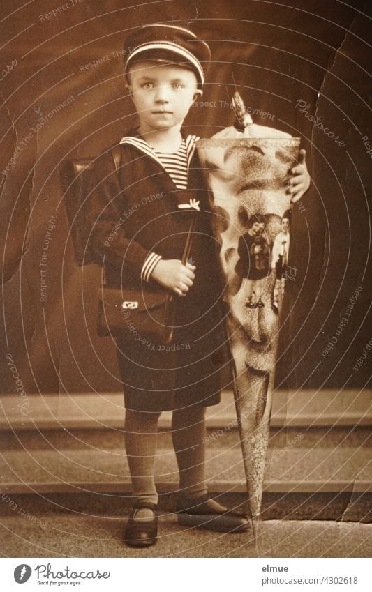 Das zerknitterte, vergilbte Papierbild aus den 1930er Jahren zeigt einen Schulanfänger mit Zuckertüte, Brottasche und Schulranzen im Matrosen Look / Steppke