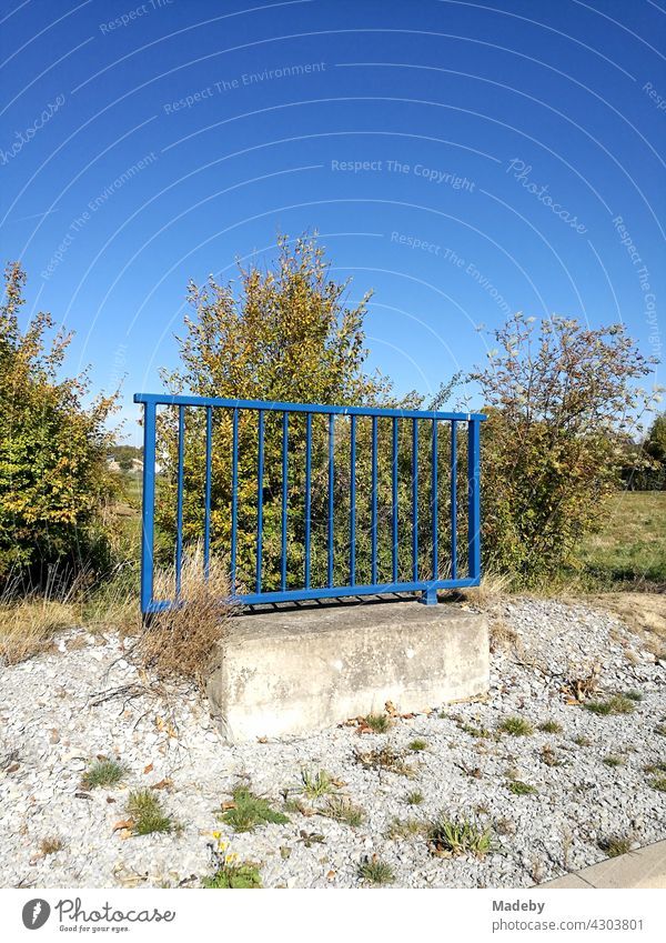 Blaues Geländer aus Stahl mit Fundament aus Beton allein auf weiter Flur vor blauem Himmel bei Sonnenschein in Oelde bei Warendorf in Westfalen im Münsterland