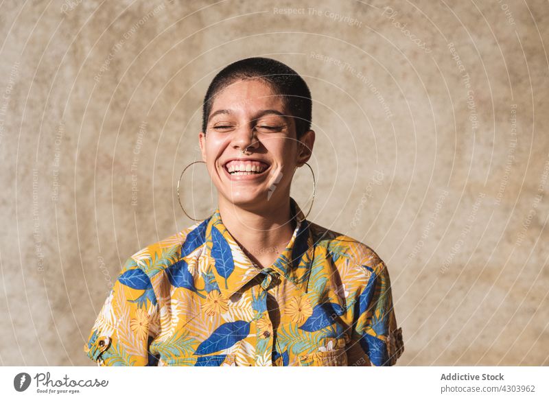 Fröhliche ethnische Frau im Hemd mit Blumenornament im Sonnenlicht heiter Lachen offen Stil geblümt Ornament freundlich Porträt Individualität bisexuell