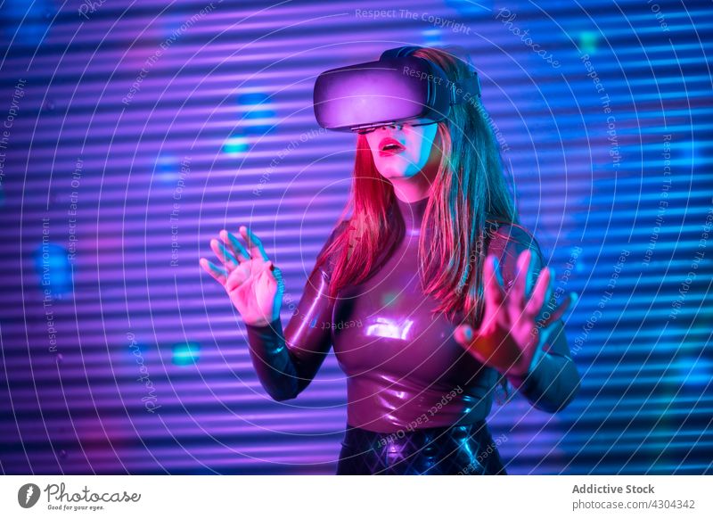 Junge Frau erkundet virtuelle Realität VR erkunden interagieren Headset gestikulieren eintauchen neonfarbig leuchten futuristisch jung Schutzbrille Innovation