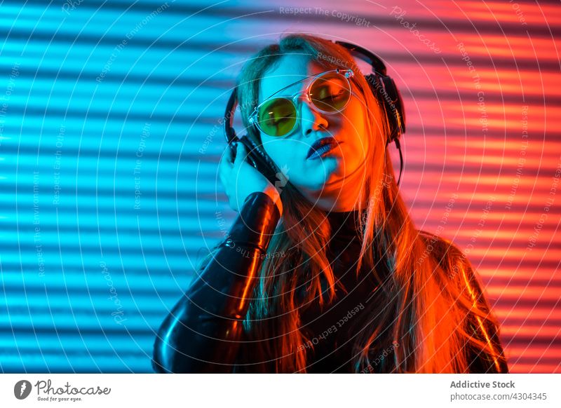 Frau hört Musik unter Neonbeleuchtung zuhören Lächeln neonfarbig blau rot leuchten modern unterhalten hell jung gestikulieren Freude Apparatur Kopfhörer Klang
