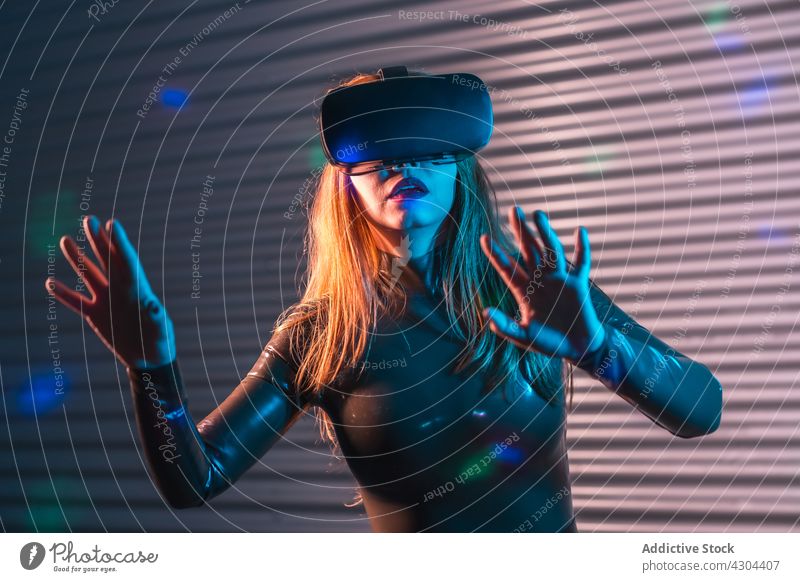 Junge Frau erkundet virtuelle Realität VR erkunden interagieren Headset gestikulieren eintauchen neonfarbig leuchten futuristisch jung Schutzbrille Innovation