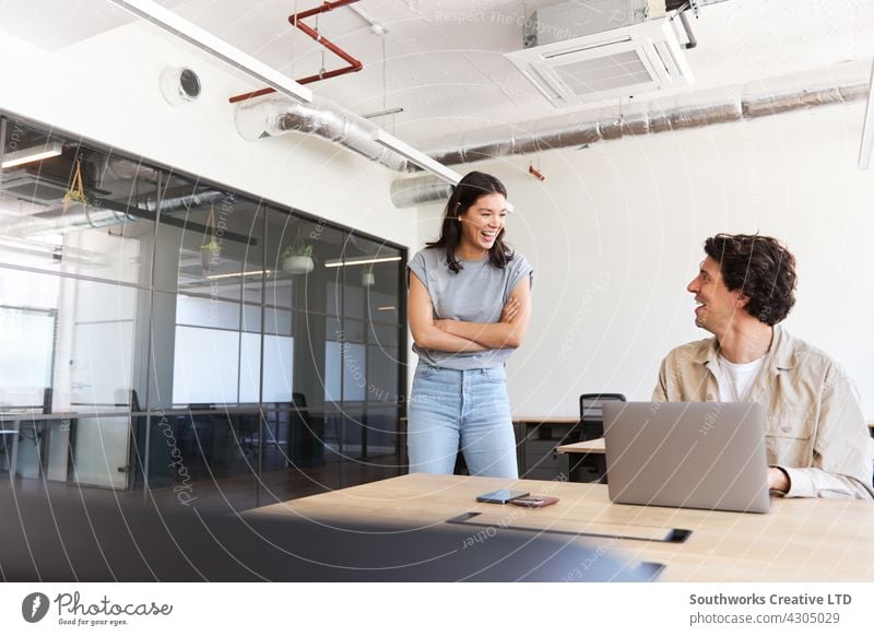 Junges Paar, das Arbeitsraum für ein Start-up-Unternehmen mietet, flirtet am Schreibtisch im Großraumbüro Frau Mann jung Büro Sitzung informell lässig sprechend