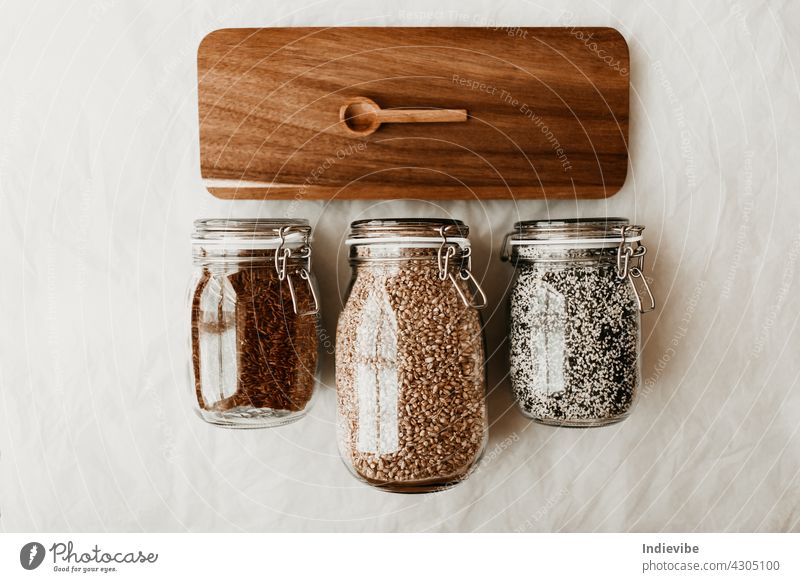Gläser mit getrockneten, ungekochten Lebensmittelzutaten und Holzlöffel auf braunem Tablett Glas vereinzelt hölzern Container weiß Samen Flasche Bestandteil